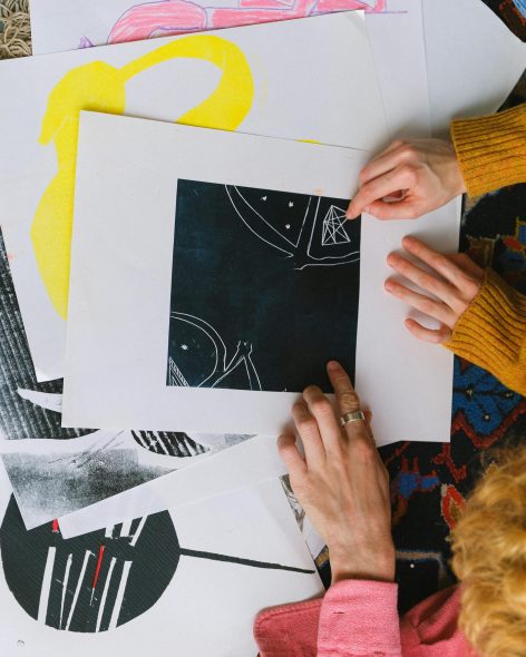 From above of unrecognizable artists working on new project together discussing abstract graphic sketch sitting at table