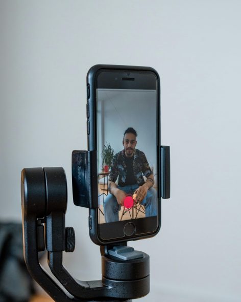 Close-up of a man recording a TikTok video using a smartphone on a stabilizer indoors.